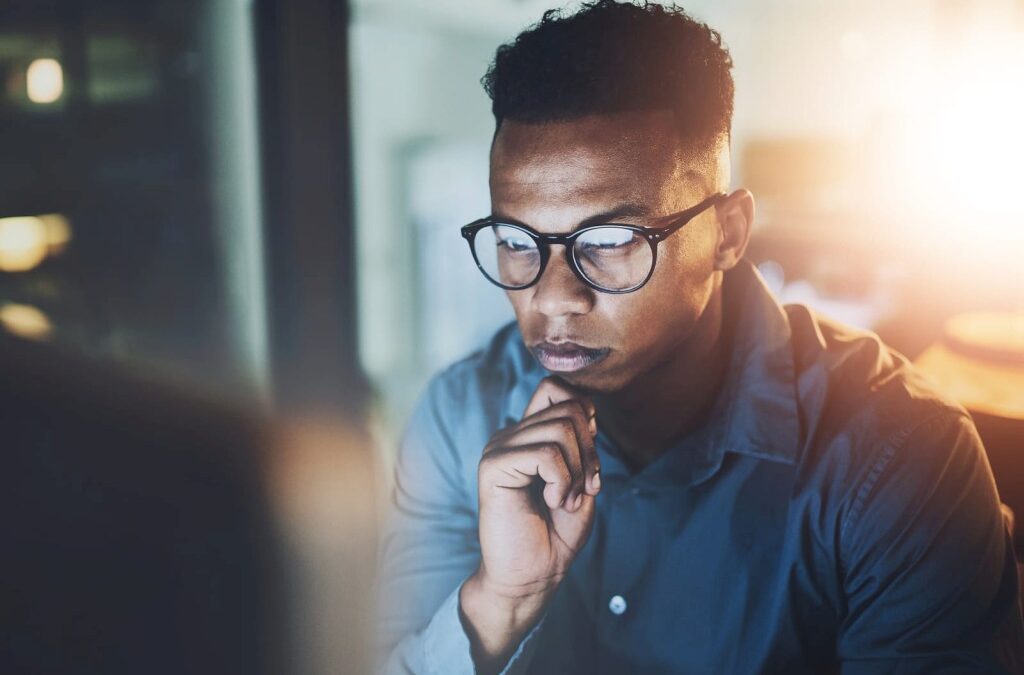 man in glasses sitting in front of a screen and thinking about something